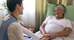 Front view of Asian female nurse taking care of senior mixed race  female patient at retirement home. Senior female is lying in bed.