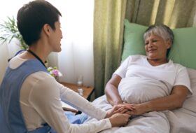Front view of Asian female nurse taking care of senior mixed race  female patient at retirement home. Senior female is lying in bed.