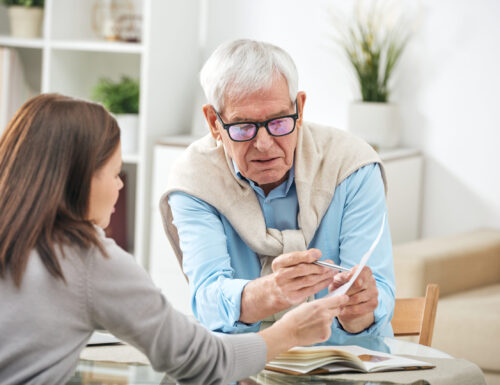 Young social worker or insurance agent asking questions of senior man about points of the paper during home consultation